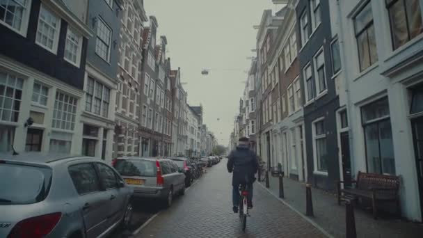 AMSTERDAM, NETHERLANDS - DECEMBER 26, 2017. Man cycling along typical street of the city — Stock Video