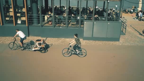 GARANTIA, POLÓNIA - 8 de abril de 2018. Filmagem em câmera lenta de ciclismo familiar com um trailer de bicicleta para criança ao longo do aterro do rio Vístula — Vídeo de Stock