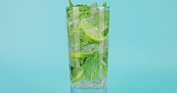 Cold sparkling mojito cocktail in a glass against blue background, close-up slow motion shot on Red — 图库视频影像