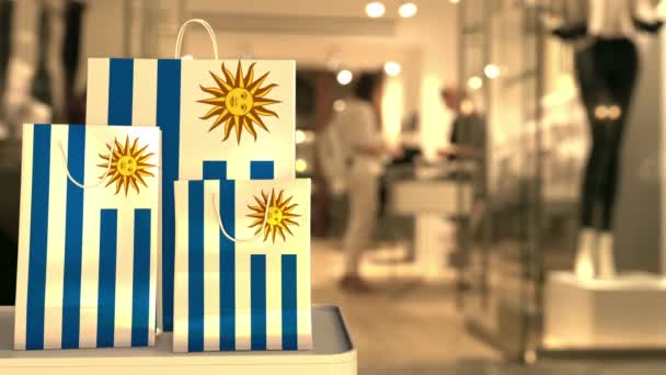 Uruguayská vlajka na papírových nákupních taškách proti rozmazanému vchodu do obchodu. Klip související s maloobchodem — Stock video