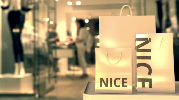 Bolsas de compras de papel con texto NICE contra tienda borrosa. Francés compras relacionadas clip — Vídeos de Stock