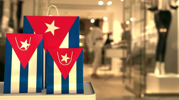 Bandera de Cuba en las bolsas de compras de papel contra la entrada borrosa de la tienda. Renderizado 3D relacionado al por menor — Foto de Stock