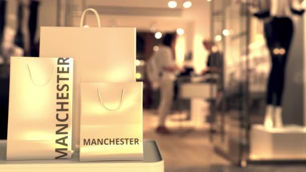 Papírové nákupní tašky s popiskem Manchesteru proti rozmazanému vchodu do obchodu. Retail in the United Kingdom related concept 3d animation — Stock video