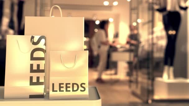 Nákupní tašky s titulem Leeds proti rozmazanému vchodu do obchodu. Retail in the United Kingdom related concept 3d animation — Stock video