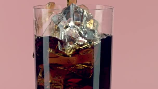 Häll cola i ett glas med isbitar på rosa bakgrund, slow motion skott på röd — Stockvideo