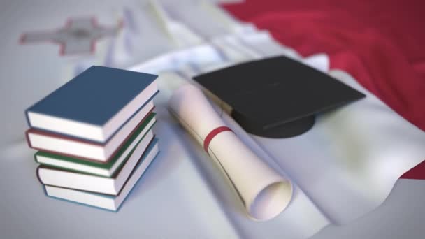Boné de formatura, livros e diploma na bandeira maltesa. Educação superior em Malta — Vídeo de Stock