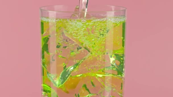 Verter refresco amarillo en un vaso con cubitos de hielo sobre fondo rosa, toma de cámara lenta sobre rojo — Vídeo de stock
