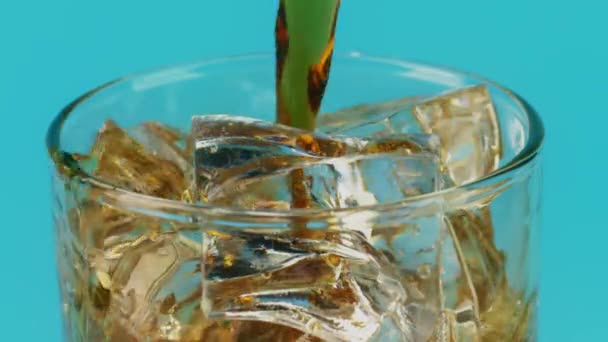 Pouring cola soft drink into a glass with ice cubes on cyan background, slow motion shot on Red — ストック動画