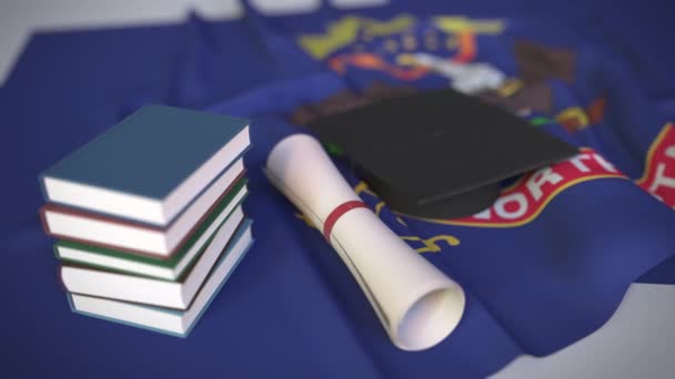 Végzős sapka, könyvek és oklevelek Észak-Dakota zászlóján. Felsőoktatás az Egyesült Államokkal kapcsolatos koncepció 3D animáció — Stock videók