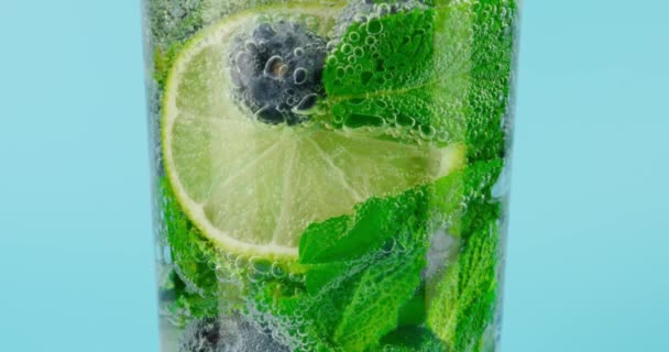 Erfrischender Cocktail mit Minze und Beeren im Glas vor hellblauem Hintergrund, Makro-Zeitlupe auf Rot — Stockvideo