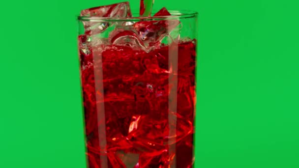 Наливание красного напитка в стакан с кубиками льда на зеленом фоне, крупным планом замедленной съемки на Красном — стоковое видео
