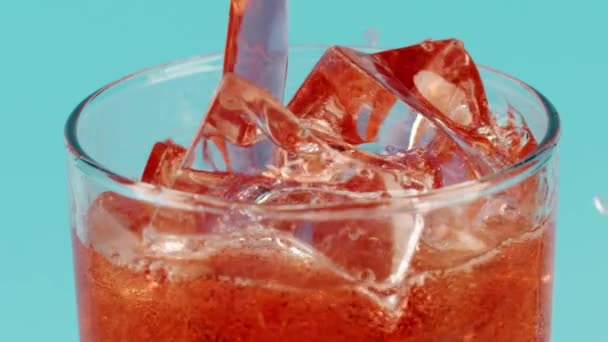 Derramando bebida vermelha em um copo com cubos de gelo contra fundo ciano, close-up tiro em câmera lenta no vermelho — Vídeo de Stock