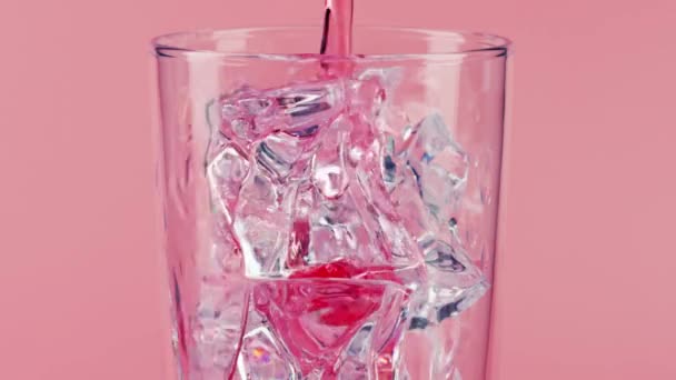 Derramando bebida rosa en un vaso con hielo sobre fondo rosa, primer plano de cámara lenta en Red — Vídeos de Stock