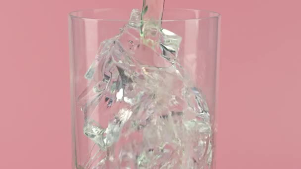 Drinken in een glas vol ijsblokjes tegen een roze achtergrond, slow motion shot op Red — Stockvideo