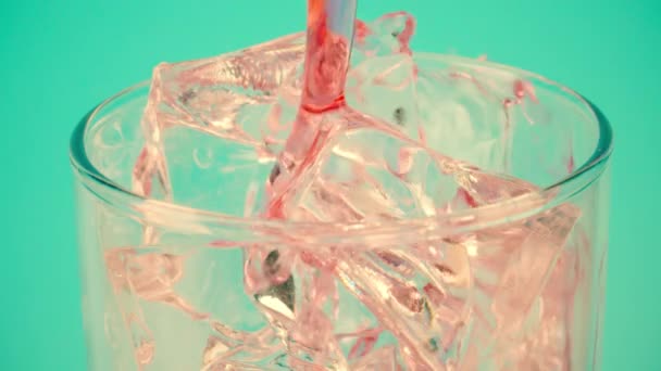 Pouring red drink into a glass with ice cubes against cyan background, close-up shot on Red — 비디오