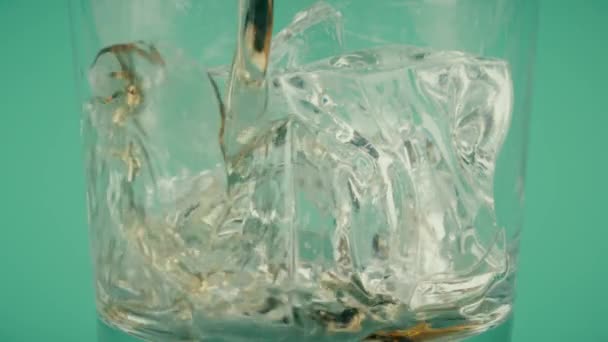 Наливание коричневого напитка в стакан с кубиками льда на зеленом фоне, замедленная съемка на Красном — стоковое видео