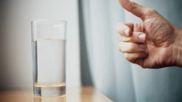 Man throws effervescent medication or vitamin pill into glass of water, slow motion shot — Stock Video
