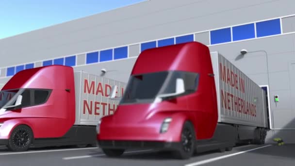 Caminhões de reboque com texto MADE IN PAÍSES BAIXOS sendo carregados ou descarregados no armazém. Animação 3D loopable relacionada com negócios holandeses — Vídeo de Stock