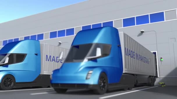 Modernos camiones semirremolques con texto MADE IN PAKISTAN siendo cargados o descargados en el almacén. Animación en 3D loopable relacionada con el negocio paquistaní — Vídeos de Stock
