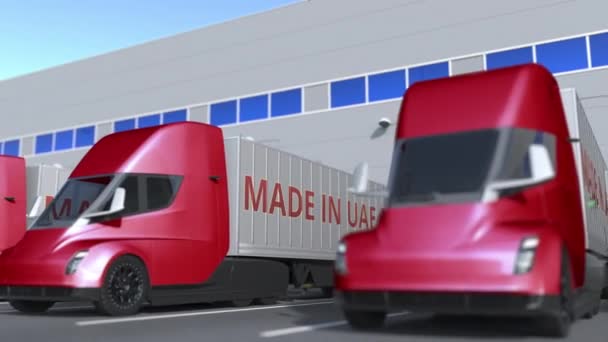 Moderne oplegger vrachtwagens met Made In Uae tekst wordt geladen of gelost in het magazijn. Verenigde Arabische Emiraten business gerelateerde loopable 3d animatie — Stockvideo