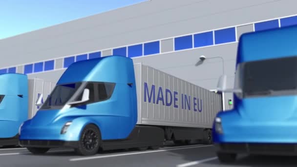 Camiões semi-reboques modernos com texto MADE IN EU a ser carregado ou descarregado no armazém. Animação 3D loopable relacionada com as empresas da União Europeia — Vídeo de Stock