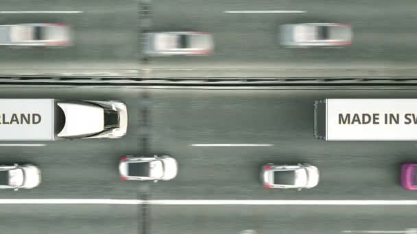 Vista aérea de camiones semirremolques con texto MADE IN SWITZERLAND conduciendo a lo largo de la carretera. Animación 3D loopable relacionada con el negocio suizo — Vídeo de stock