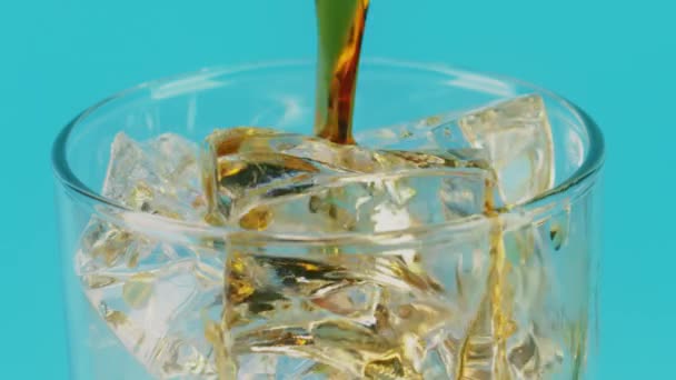 Versare la cola in un bicchiere pieno di cubetti di ghiaccio su sfondo ciano, macro scatto al rallentatore su Red — Video Stock