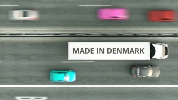 Вид сверху вниз на полуприцепы с текстом MADE IN DENMARK, движущимися по дороге. Цифровая 3D анимация в Дании — стоковое видео