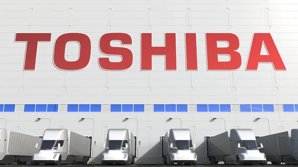 Caminhões semi-reboque elétricos na baía de carregamento do armazém com logotipo TOSHIBA na parede. Renderização 3D editorial — Fotografia de Stock