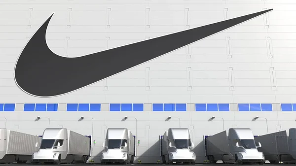 Electric semi-trailer trucks at warehouse loading bay with NIKE logo on the wall. Editorial 3D rendering — Stock Photo, Image