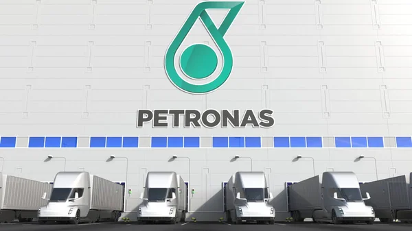 Электрические полуприцепы на складе погрузочной площадки с логотипом PETRONAS на стене. Редакционная 3D рендеринг — стоковое фото