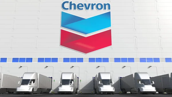 Electric semi-trailer trucks at warehouse loading bay with CHEVRON CORPORATION logo on the wall. Editorial 3D rendering — Stock Photo, Image