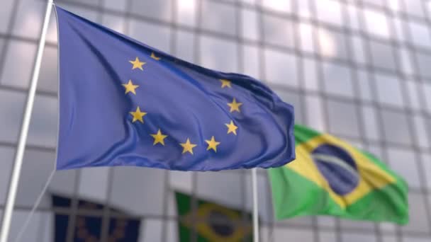 Ondeando banderas de la UE y Brasil frente a un rascacielos moderno — Vídeo de stock