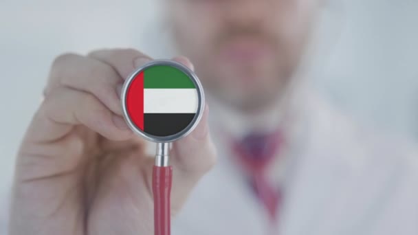 El doctor sostiene la campana del estetoscopio con la bandera de los EAU. Salud en los Emiratos Árabes Unidos — Vídeo de stock