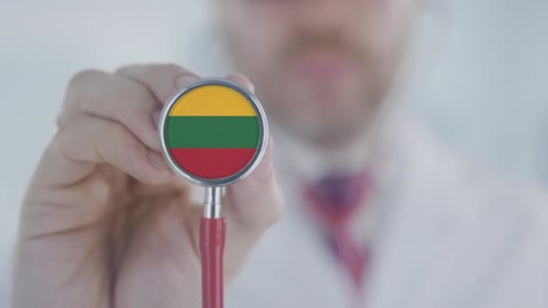 Doktor trzyma dzwonek stetoskopowy z litewską flagą. Opieka zdrowotna na Litwie — Wideo stockowe