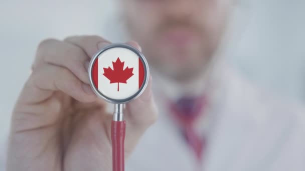 Lékař drží stetoskop zvonek s kanadskou vlajkou. Healthcare in Canada — Stock video