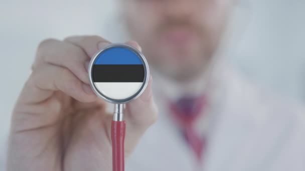 El doctor sostiene la campana del estetoscopio con la bandera estonia. Salud en Estonia — Vídeo de stock
