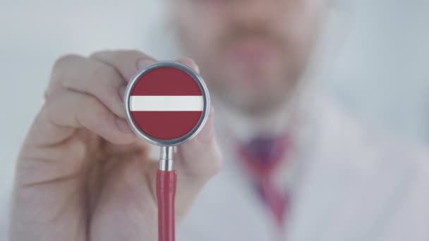 Doctor escuchando con el estetoscopio con la bandera de Letonia. Sanidad letona — Vídeo de stock