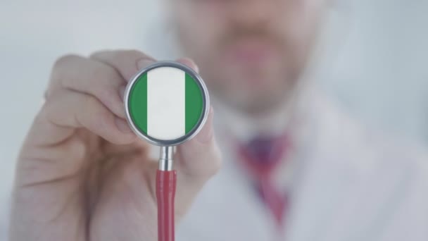 Lekarz medycyny trzyma dzwonek stetoskopowy z nigeryjską flagą. Opieka zdrowotna w Nigerii — Wideo stockowe