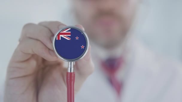 Врач держит стетоскоп с флагом страны. Здравоохранение в Новой Зеландии — стоковое видео