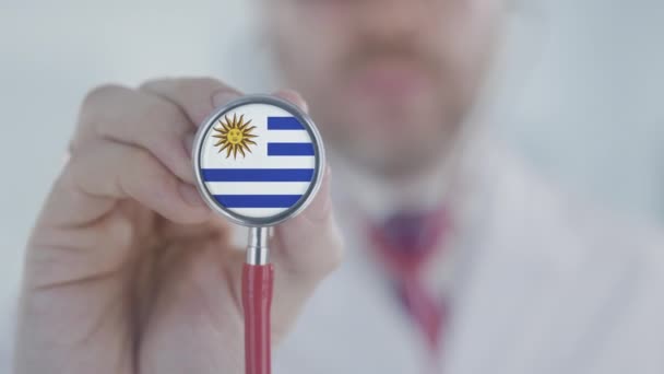 El doctor sostiene la campana del estetoscopio con la bandera uruguaya. Salud en Uruguay — Vídeo de stock