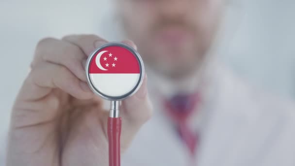 Az orvos a sztetoszkópot hallgatja szingapúri zászlóval. Szingapúr egészségügyi ellátása — Stock videók