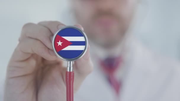 Il dottore tiene la campana dello stetoscopio con la bandiera cubana. Sanità a Cuba — Video Stock