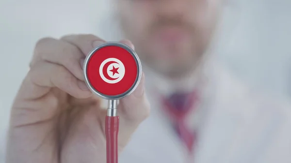 Доктор тримає дзвінок з стетоскопом з туніським прапором. Медичне обслуговування в Тунісі — стокове фото