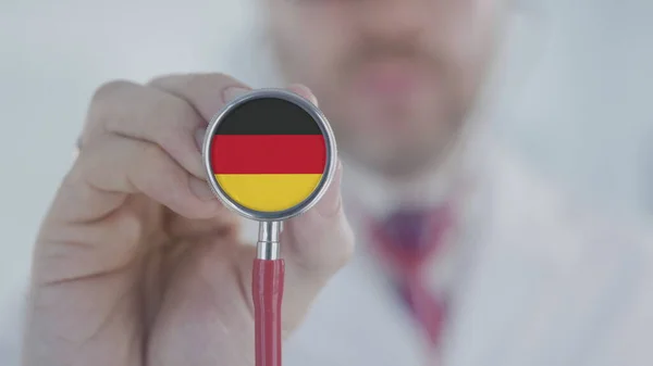 El médico sostiene la campana del estetoscopio con la bandera alemana. Salud en Alemania —  Fotos de Stock
