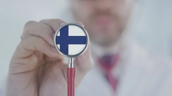 Doktor trzyma dzwonek stetoskopowy z fińską flagą. Opieka zdrowotna w Finlandii — Zdjęcie stockowe