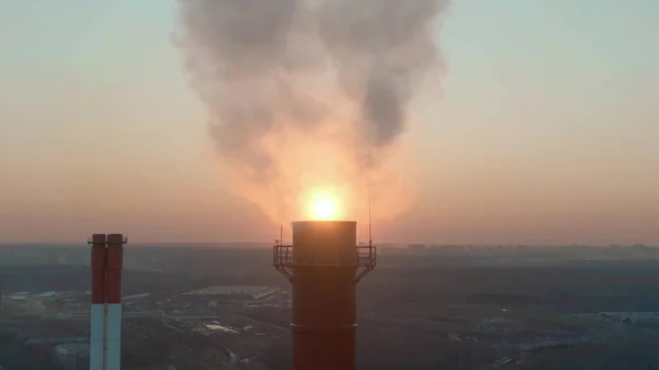 Воздушный выстрел показывает вечернее солнце за загрязняющим дымовую трубу — стоковое фото