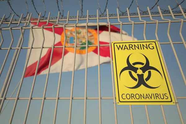 Предупреждающий знак коронавируса на заборе из колючей проволоки против флага Флориды. Карантин COVID-19 — стоковое фото
