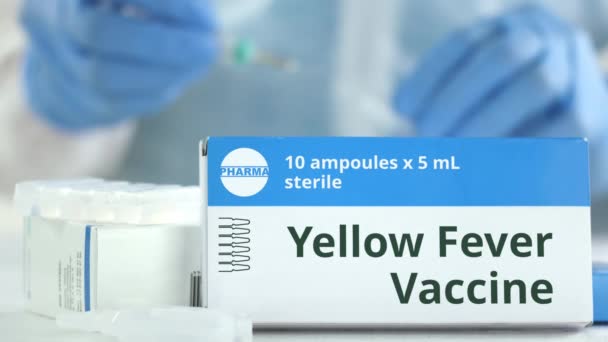 Ampuller med gula febern vaccin på bordet nära fungerande laboratorieassistent, fiktiv logotyp på lådan — Stockvideo