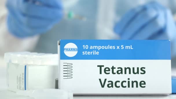 Ampullen met tetanusvaccin op tafel bij een werkende laboratoriumassistent, fictief logo op de doos — Stockvideo